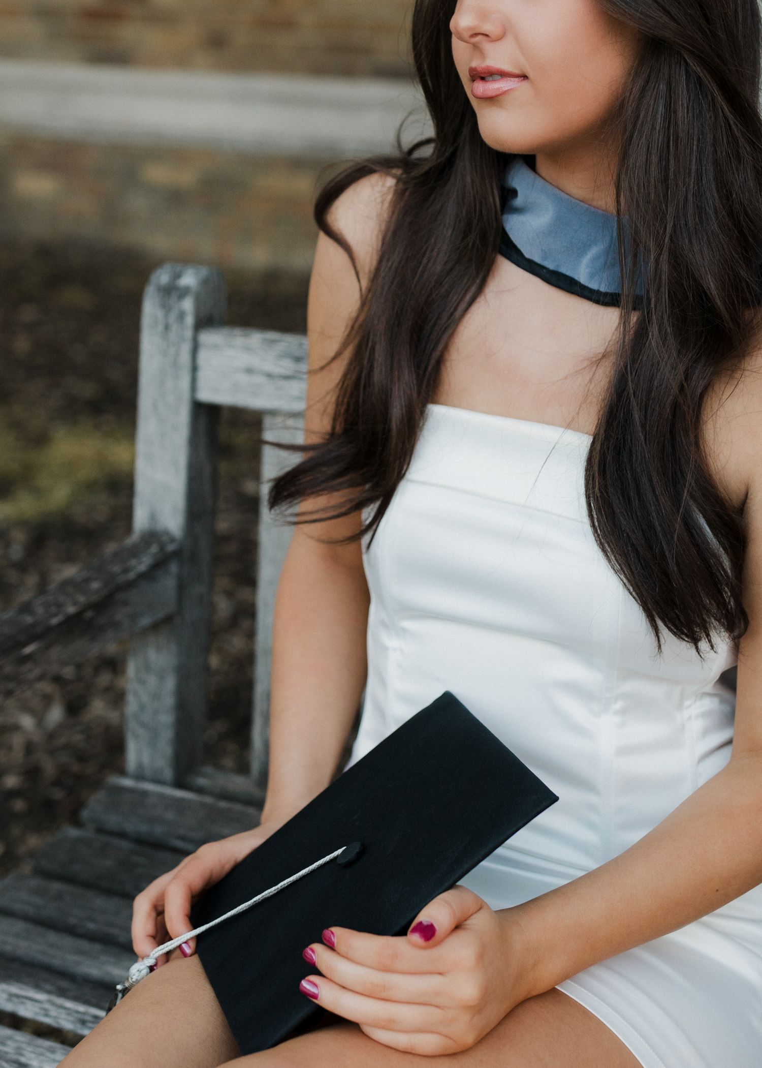 Close-up portrait showing graduate with cap wearing white dress and blue stole.