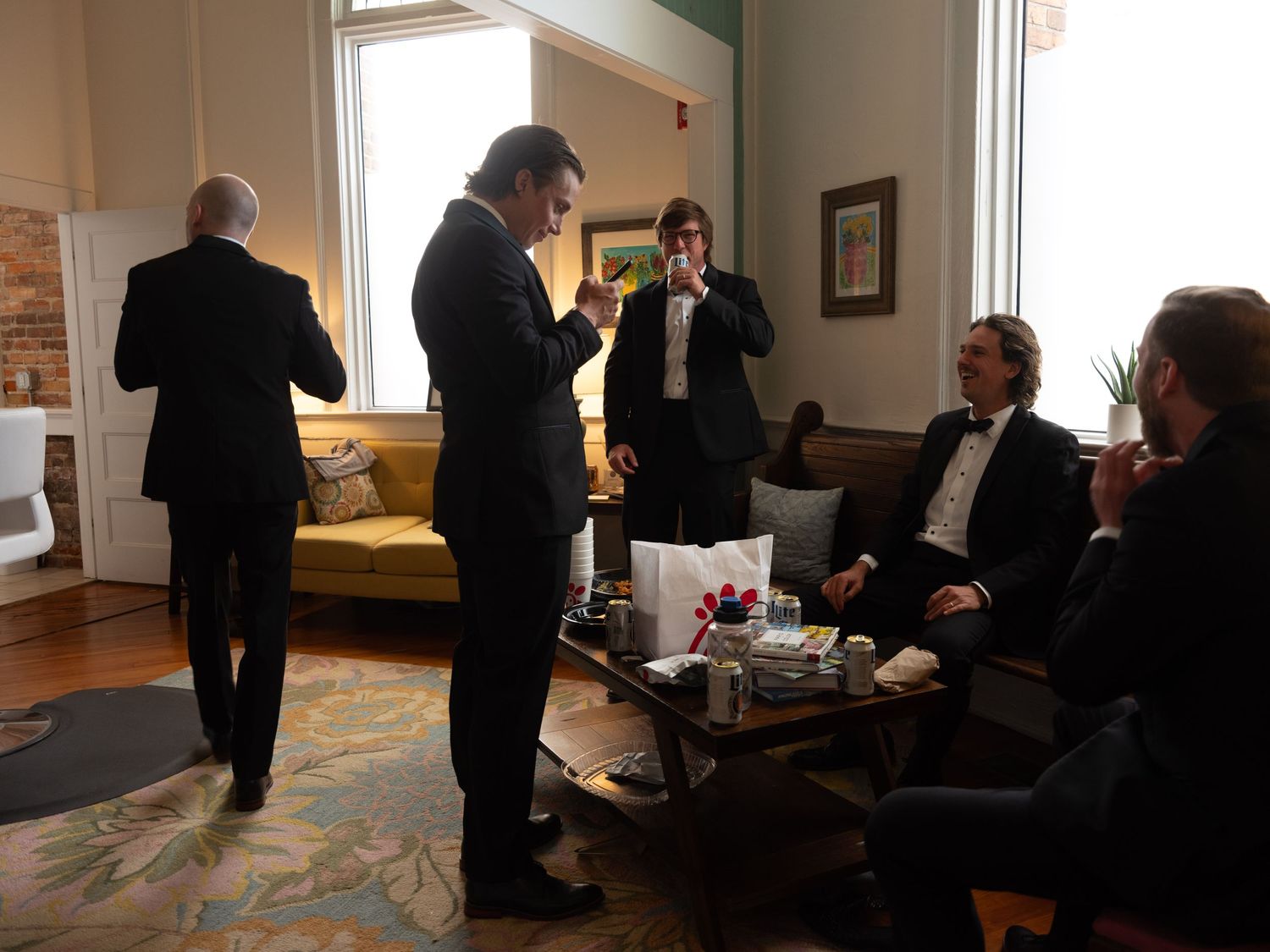People in formal attire gathered in an elegant living room with natural lighting and vintage furnishings.