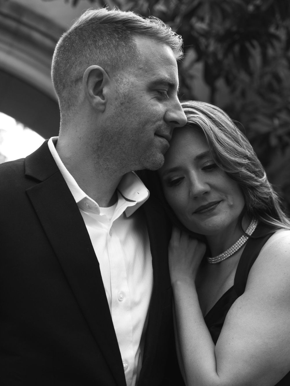 An intimate black and white portrait of a couple in formal attire sharing a tender moment.