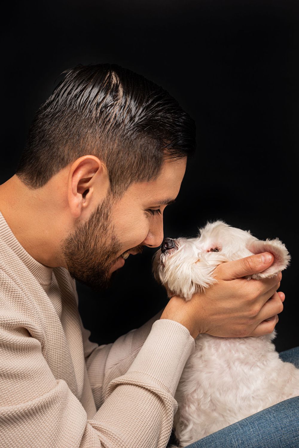 White dog and companion share intimate moment against dark background.