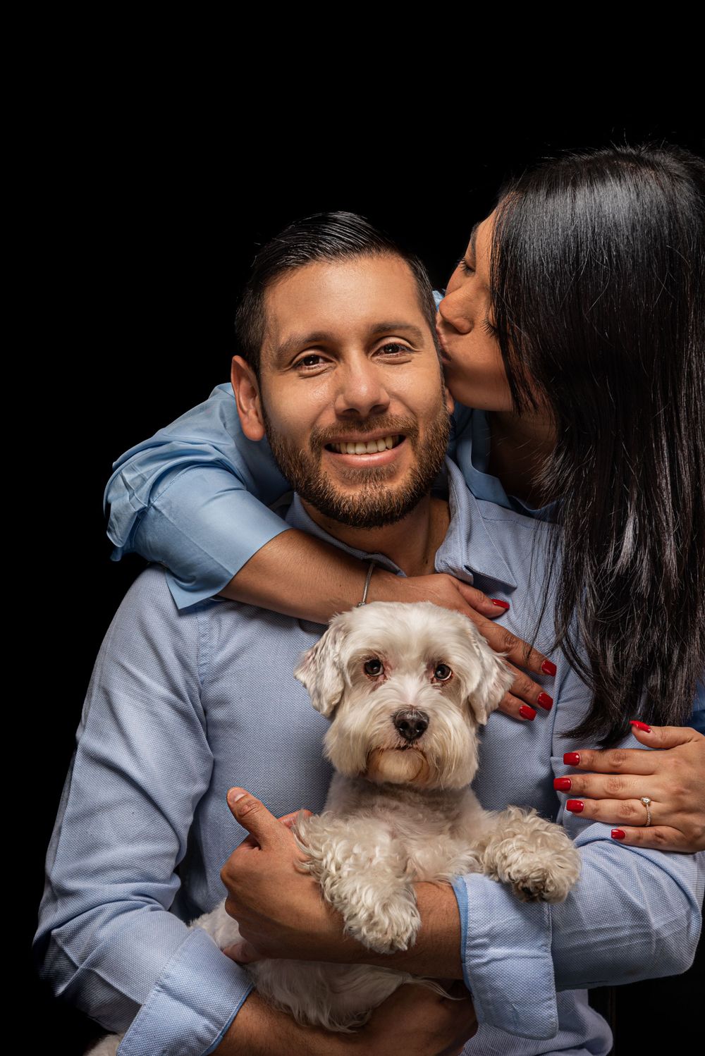 White terrier dog held while receiving affection against dark background.