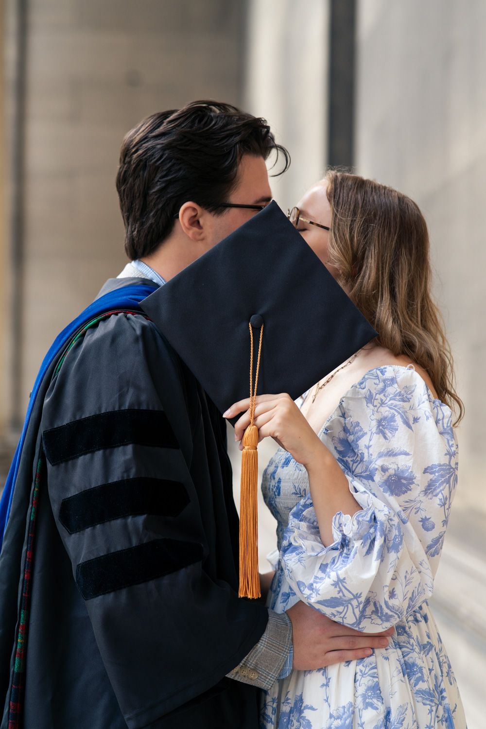A graduate in academic regalia shares a tender moment with a person in a blue and white floral dress on graduation day.