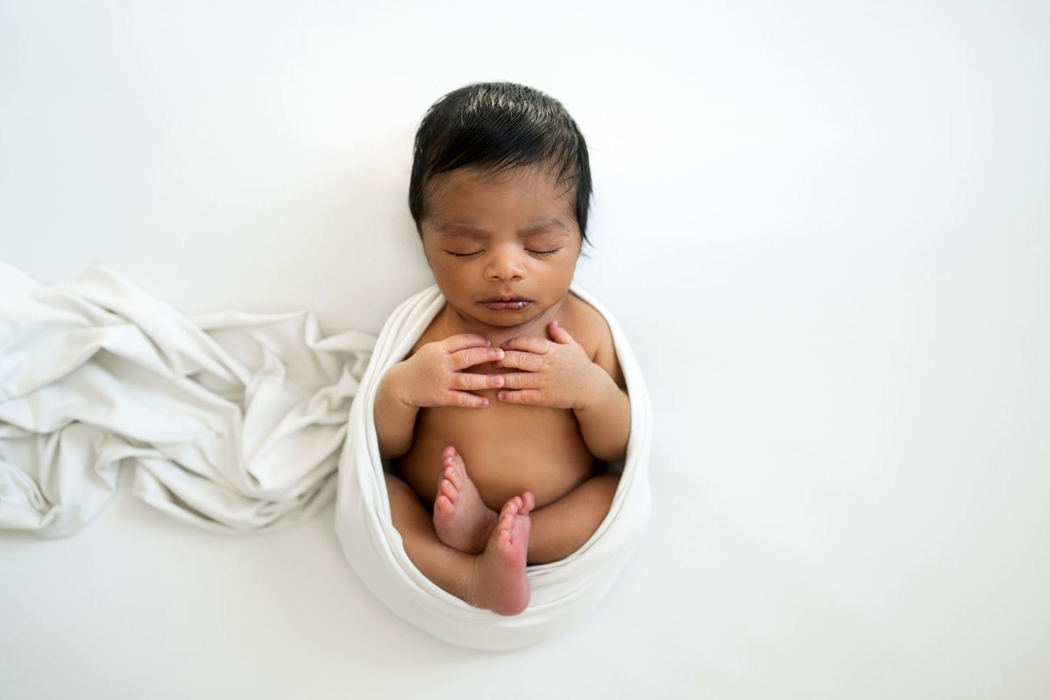 Baby wearing white headband lying on white fabric with flowing draped material.