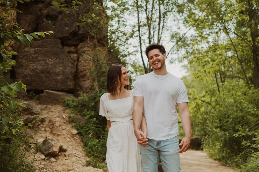 A happy couple strolls hand in hand on a nature path with rocky cliffs in the background.