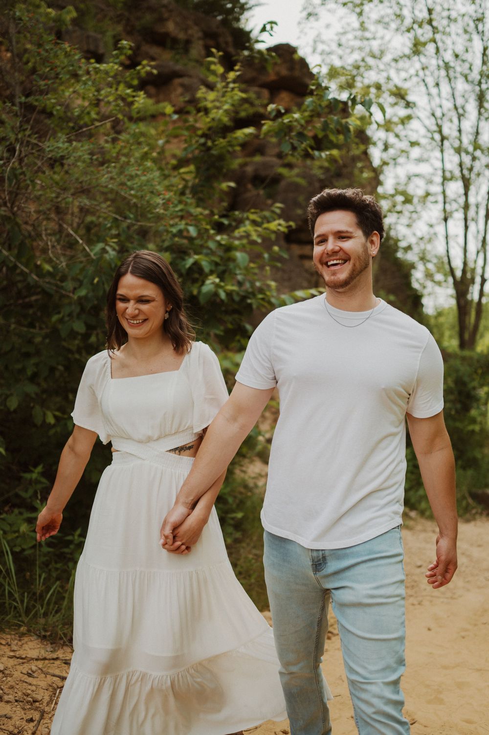 A couple shares laughter while walking together on a trail near dramatic rock formations.