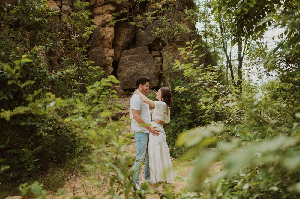 A couple embraces on a scenic nature trail with towering rock formations in the background.