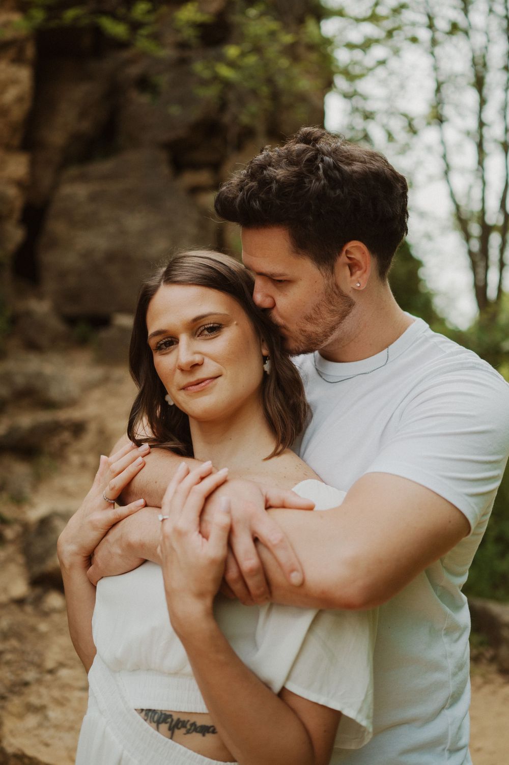 An intimate embrace captured against a backdrop of natural rock formations and trees.