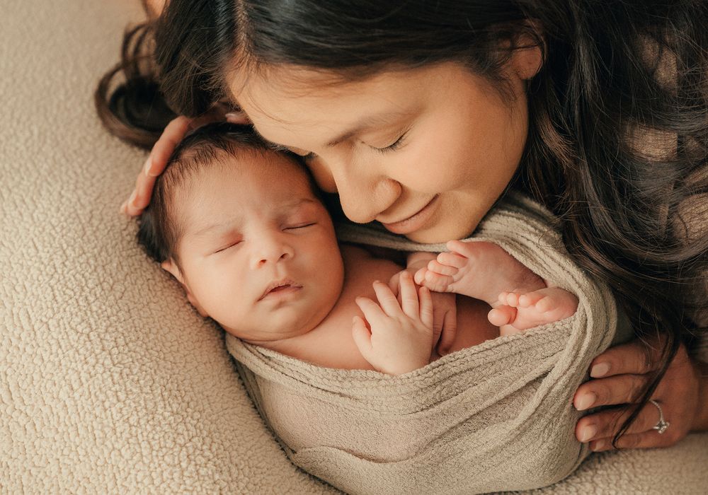 A peaceful moment captured as mother and sleeping newborn baby lie together wrapped in soft beige fabric.
