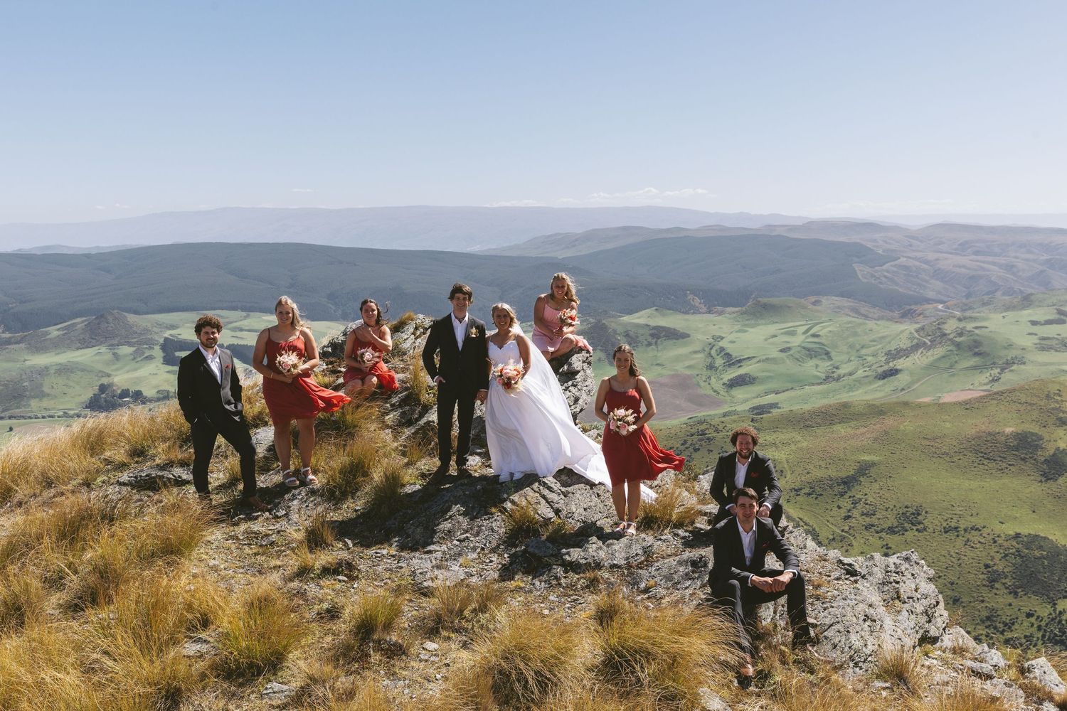Wedding party celebrates on a rocky mountaintop with sweeping views of green valleys below.