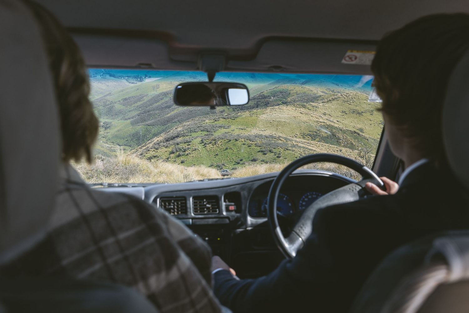 View from inside a car driving through mountainous terrain with dashboard and steering wheel visible.