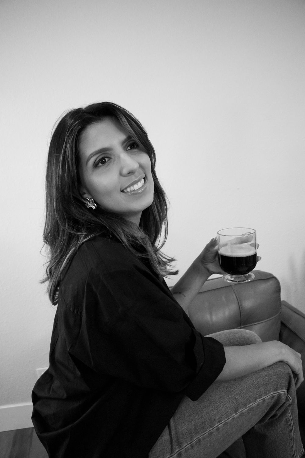 Black and white lifestyle portrait of woman with beverage on leather furniture.