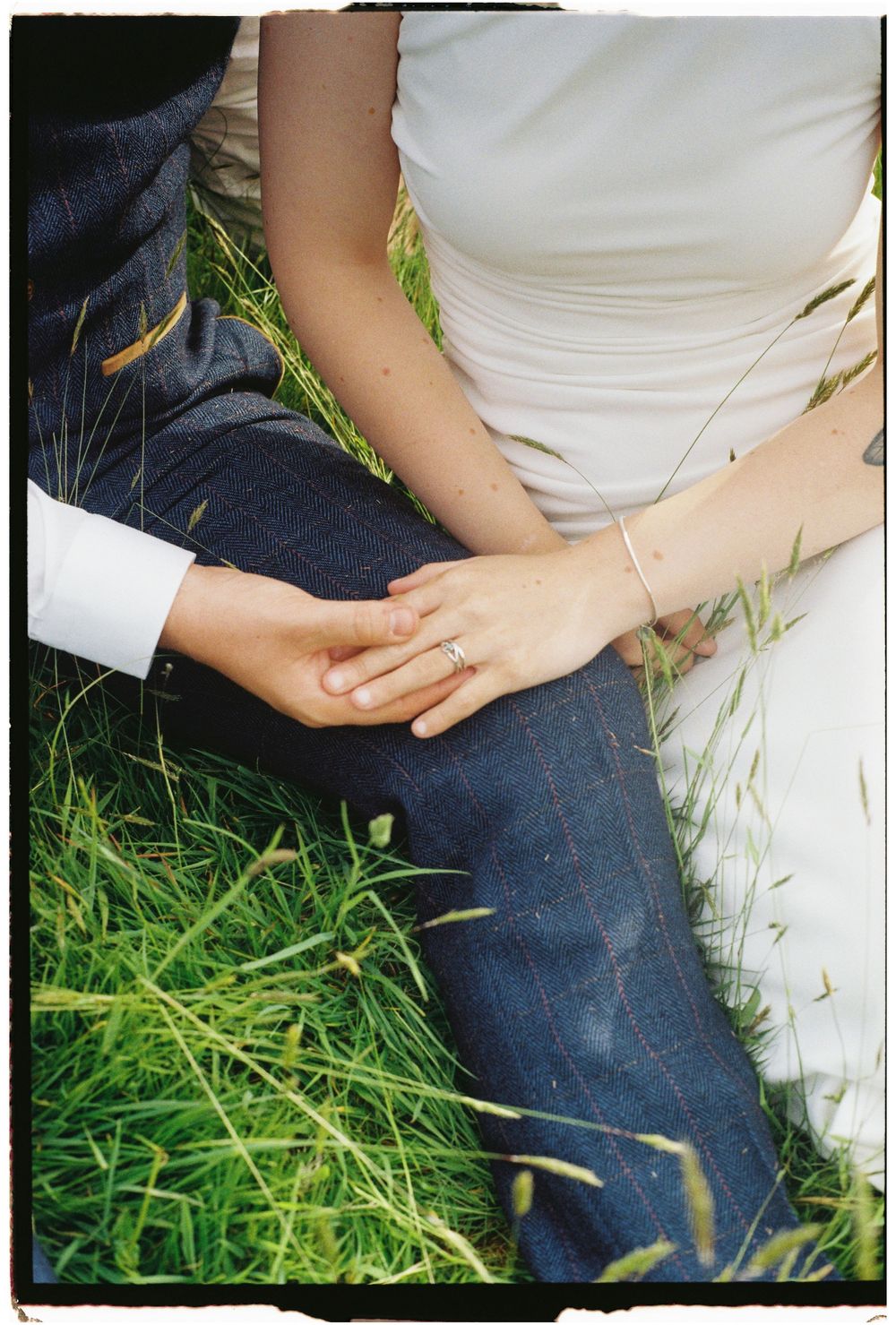 Close-up shot of hands clasped together on grass, showing a couple in wedding attire.