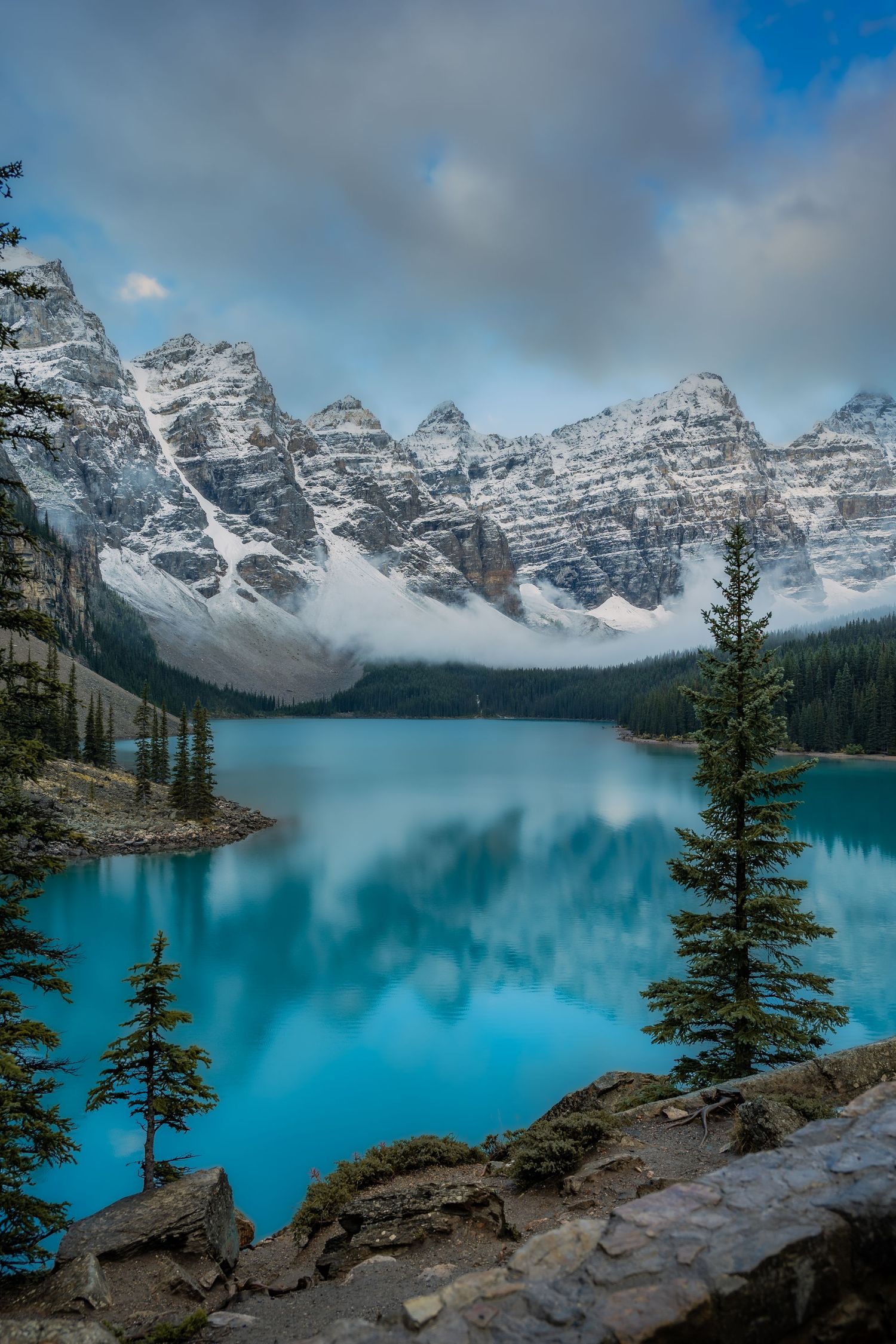 A person in purple jacket stands by Berg Lake at sunset with Mount Robson and glacier in Jasper National Park, Canada.