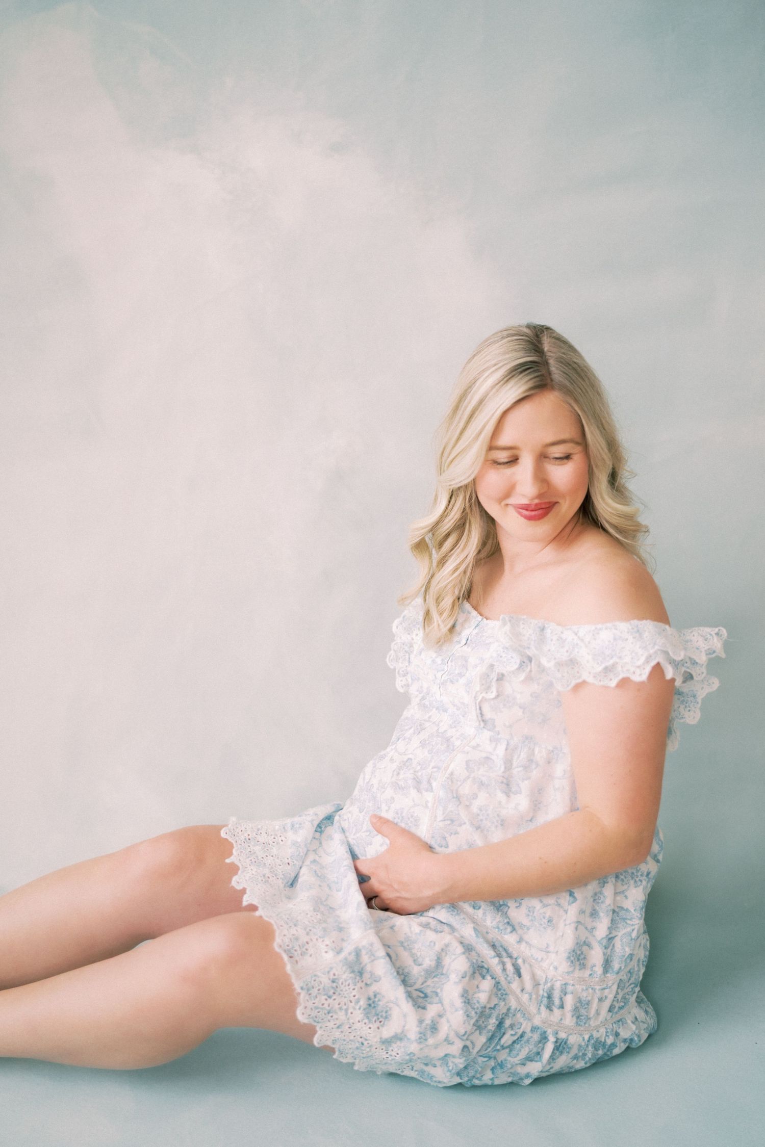 A person in a delicate off-shoulder white lace dress poses gracefully against a light blue background.