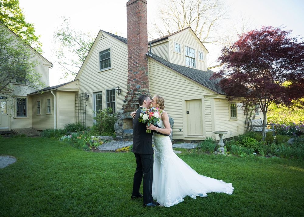 Wedding party poses on a green lawn with white colonial style houses in the background on a sunny day.