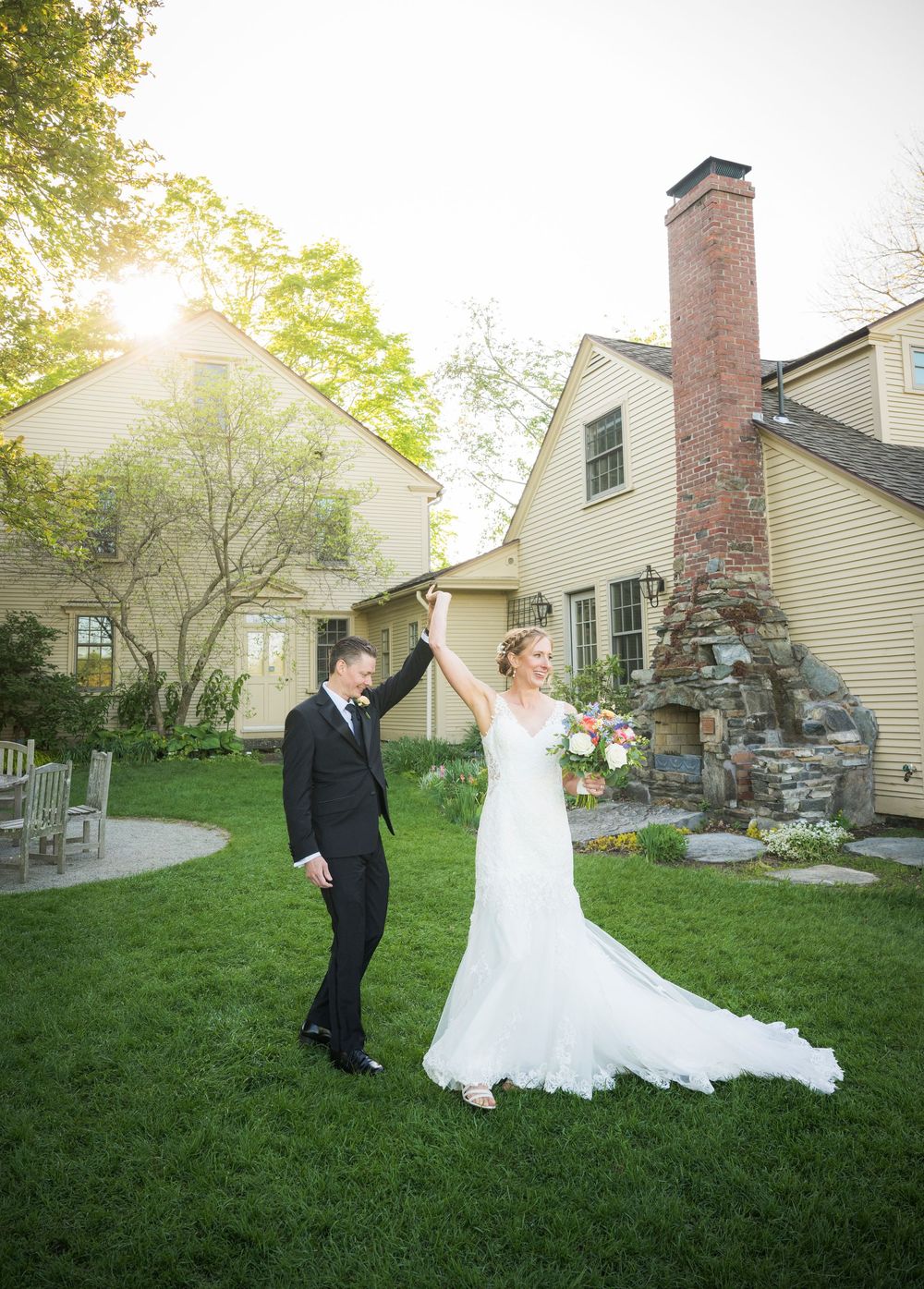 A couple sharing a celebratory moment on their wedding day in front of a charming colonial style house at sunset.