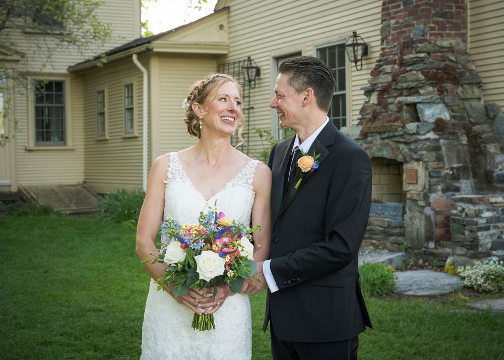 A couple shares a tender moment in front of a stone chimney and beige house exterior.