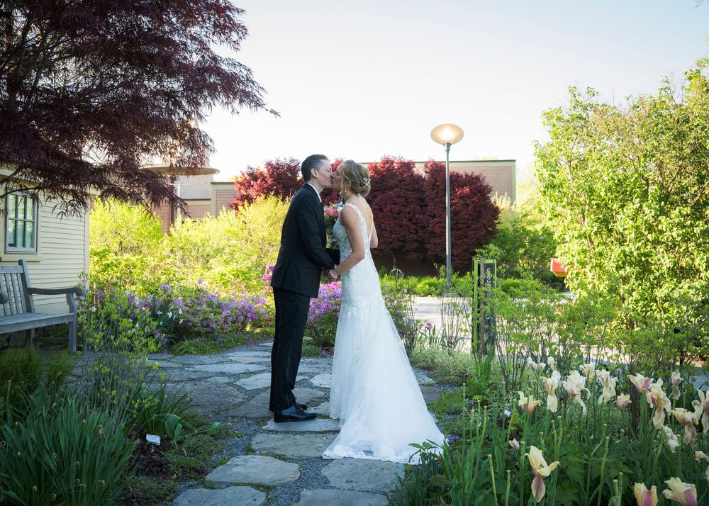 Romantic wedding couple sharing a kiss in garden setting with blooming spring flowers.