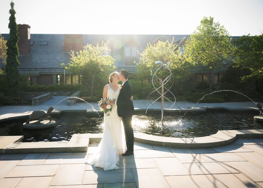 A romantic wedding moment captured at sunset on a stone patio with garden features in the background.
