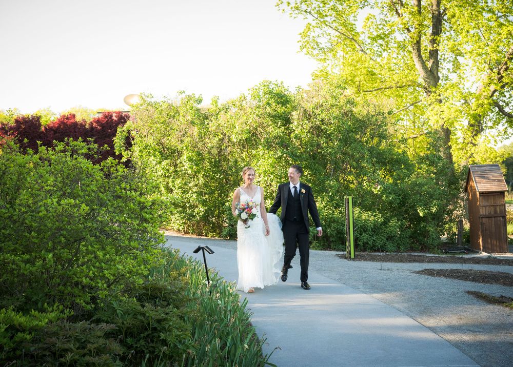 A couple walks together along a garden path surrounded by lush greenery on their wedding day.