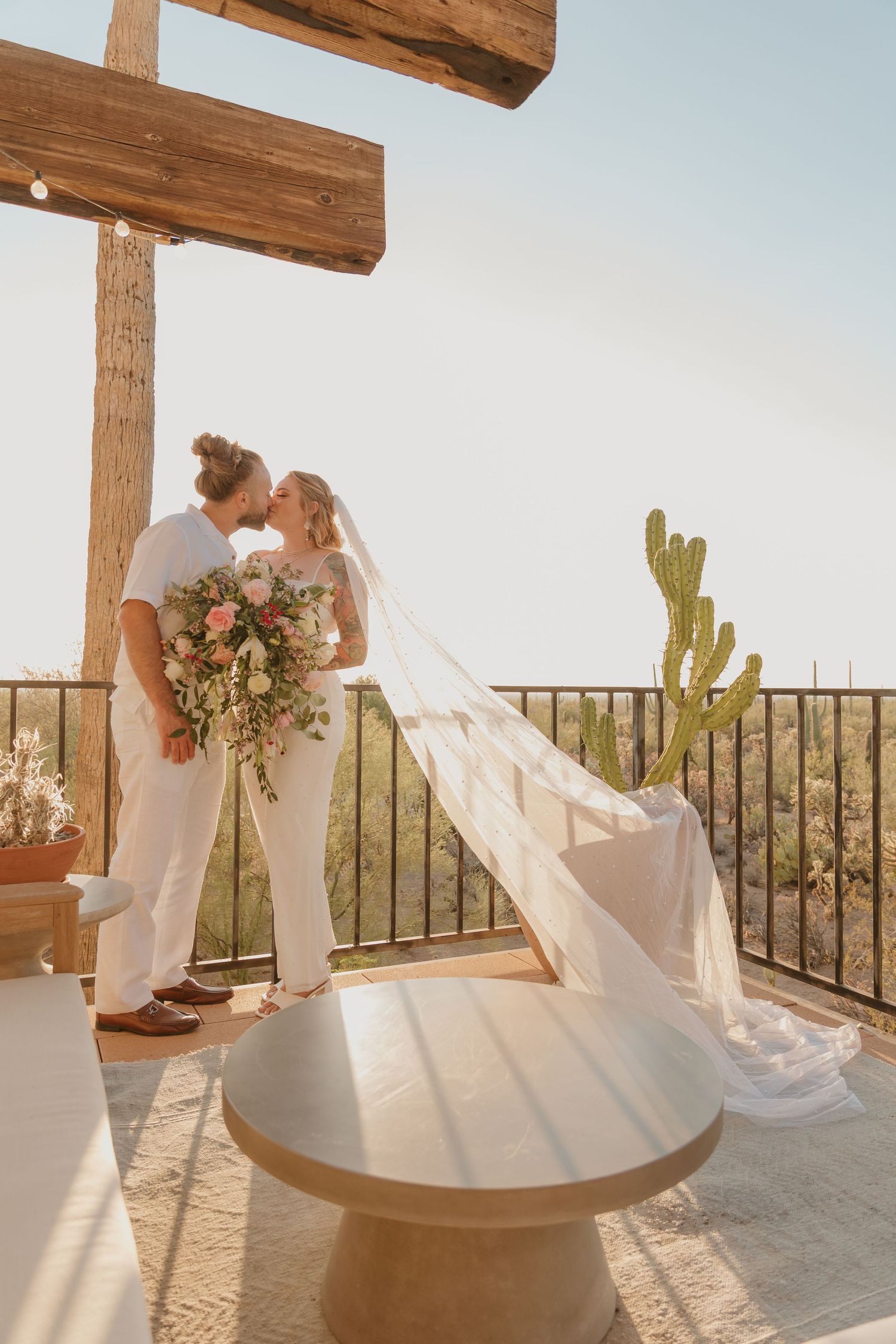 Romantic wedding couple shares intimate moments on a sun-drenched balcony with desert cactus and wooden beams overhead.