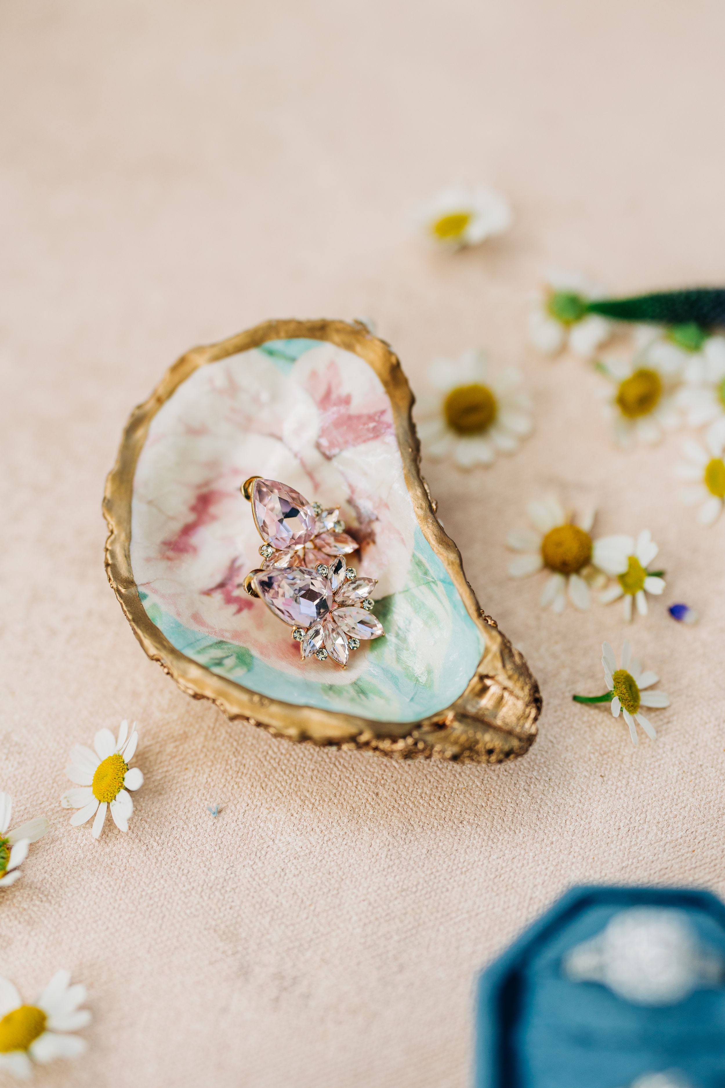 wedding flatlay with ring displayed on iridescent oyster shells with scattered white daisies on beige fabric background
