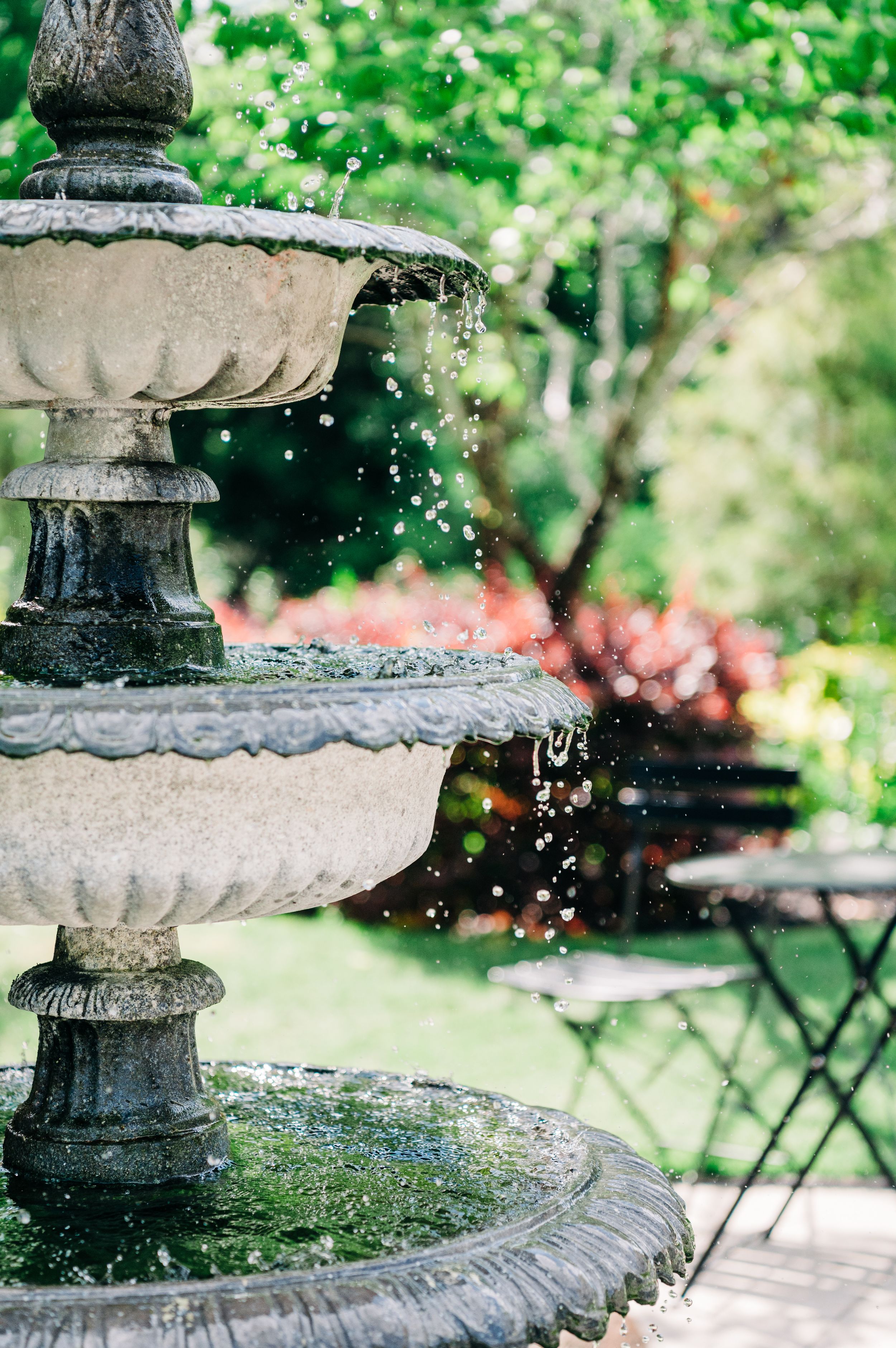 Water droplets sparkle in sunlight as they cascade down the tiers of an ornate stone garden fountain at Wildflower 301