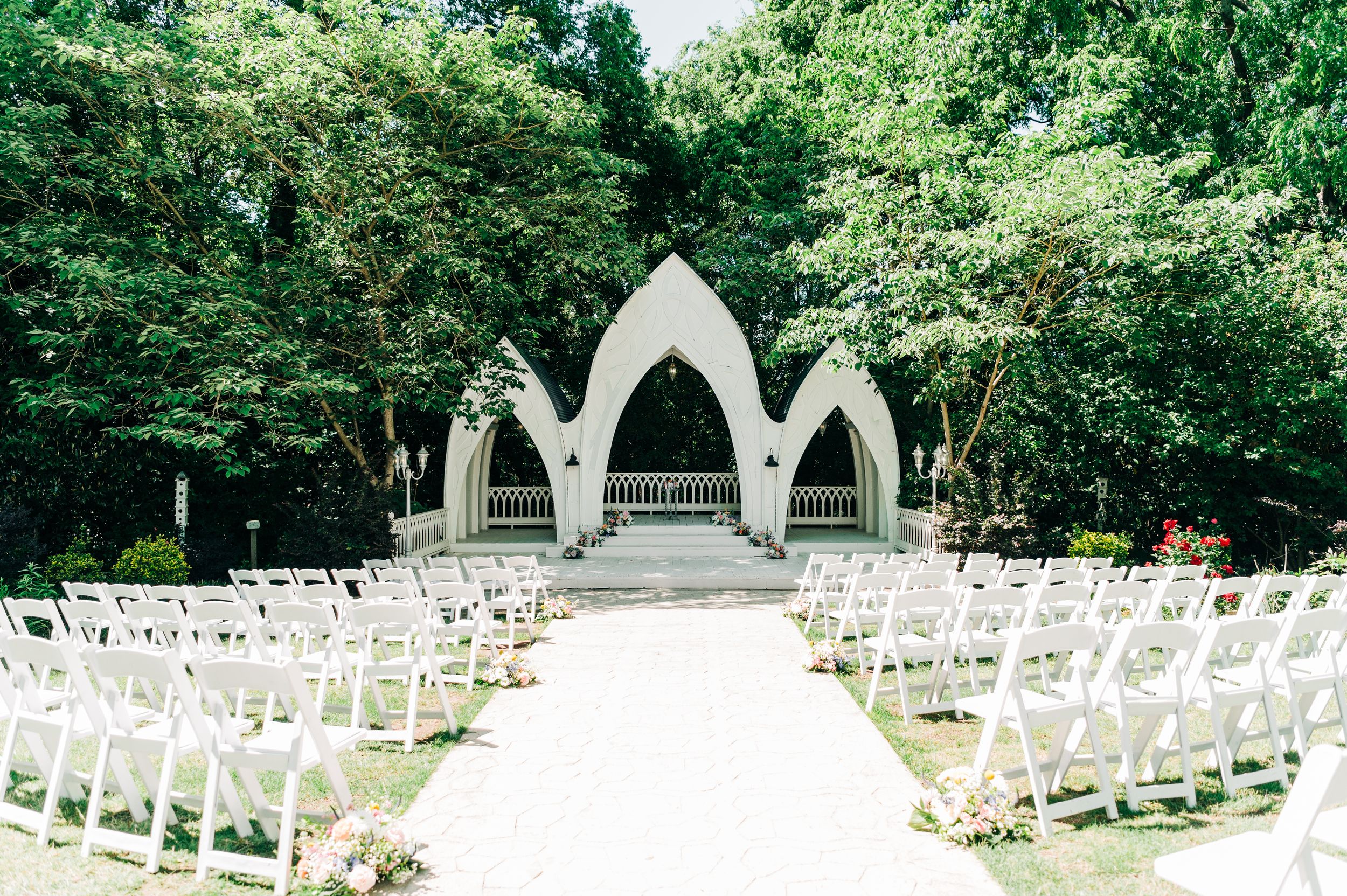White chairs line up in rows at an outdoor garden wedding venue with arched architectural features and lush greenery at the wildflower 301