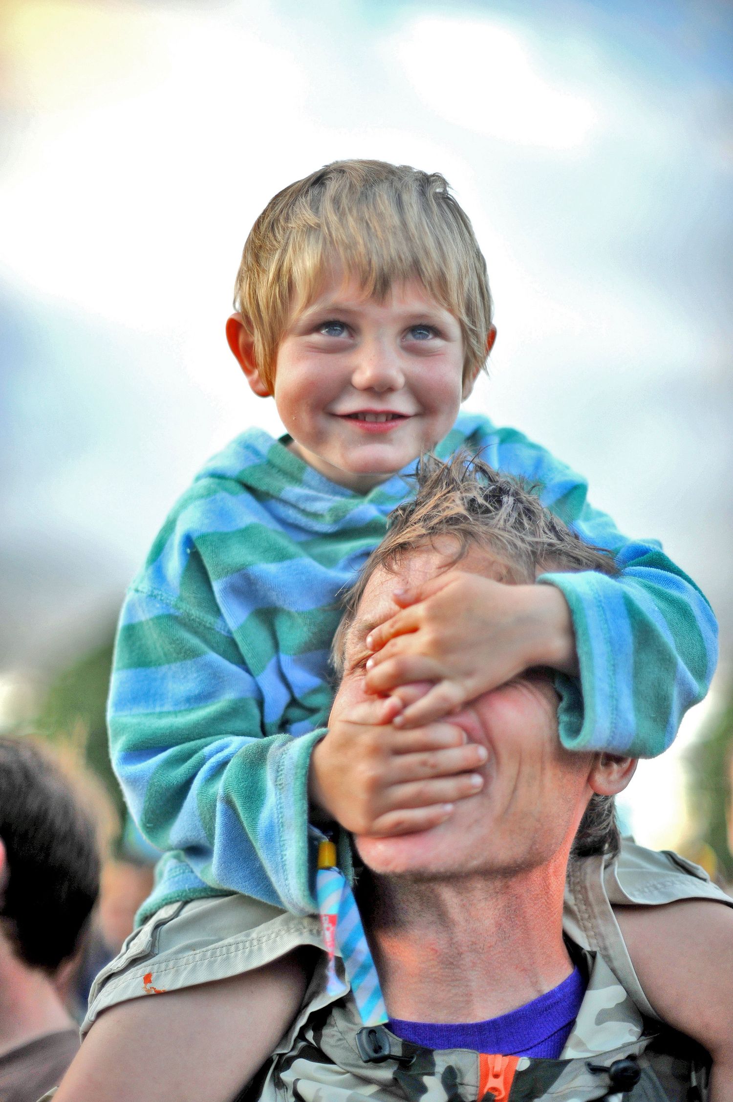 A joyful moment captured as a child in a blue tie-dye sweatshirt sits on shoulders at an outdoor event.