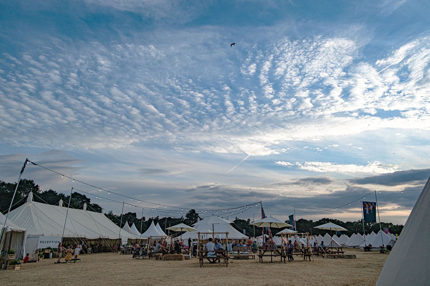 A stunning sunset sky with rippled clouds over an outdoor festival venue with white tents.