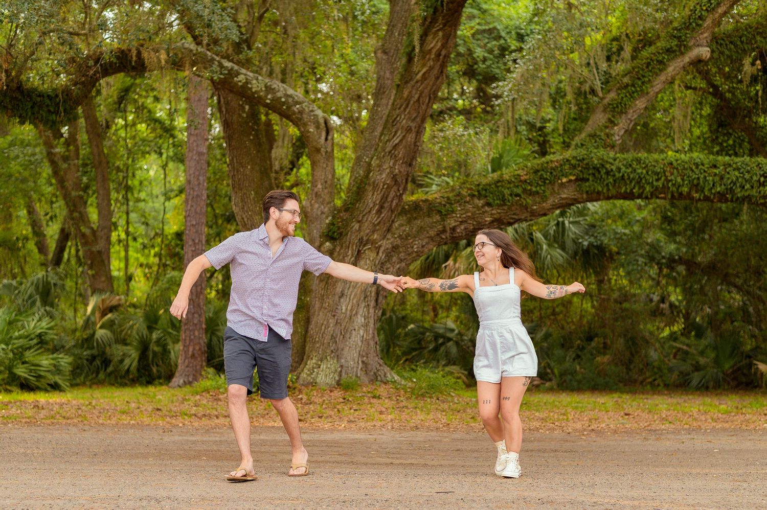 A couple dances playfully together on a tree-lined path in a park setting.