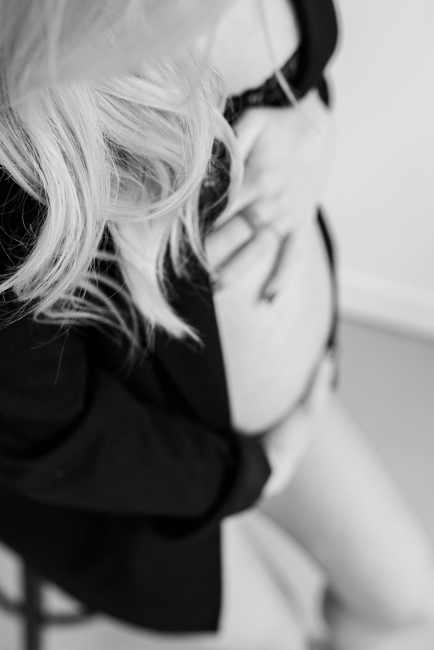 Black and white artistic portrait showing platinum blonde hair against dark clothing in soft focus.