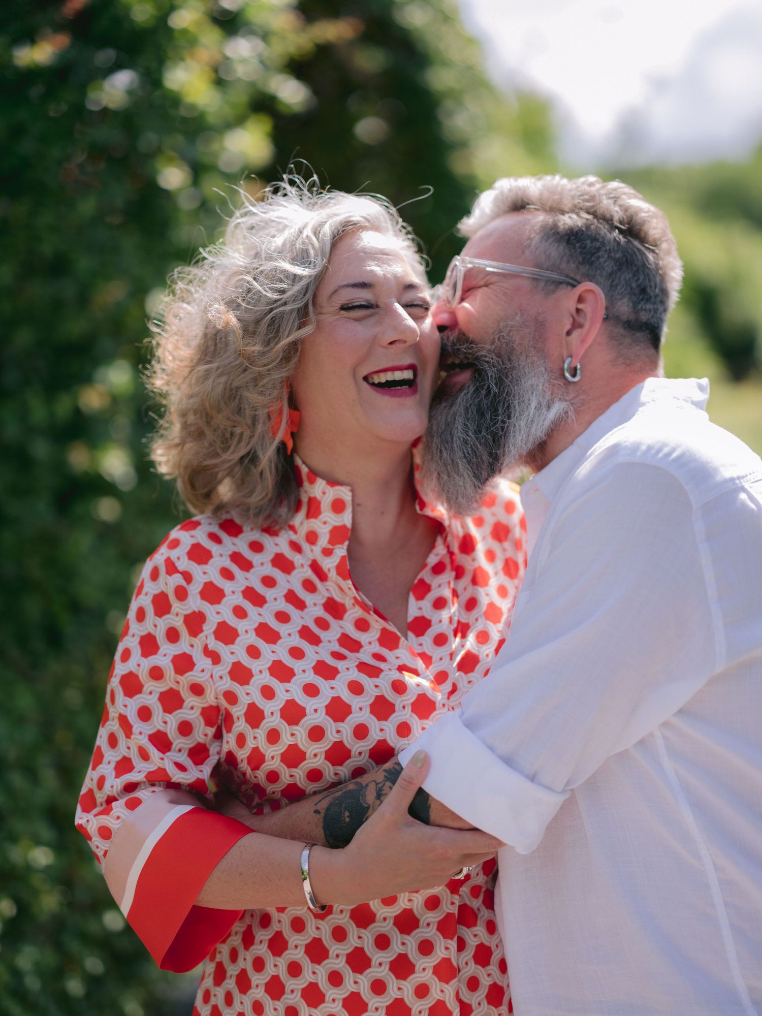 A happy couple poses in decorative garden arch while someone takes their photo on a sunny summer day.