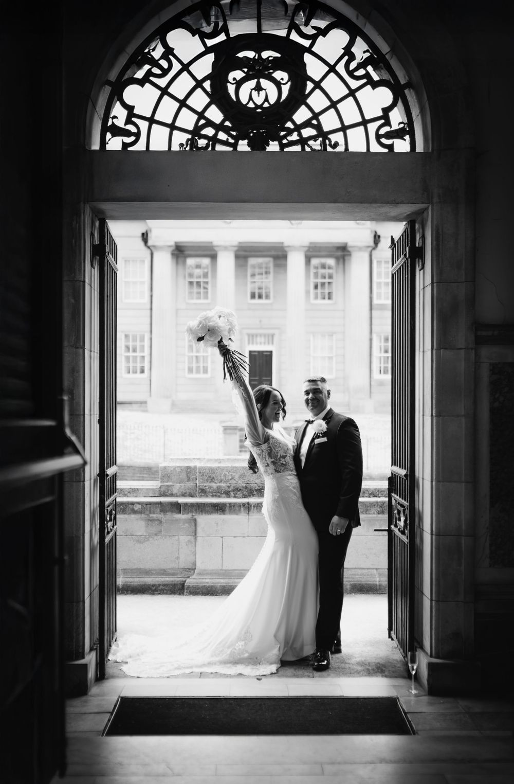 A romantic silhouette of newlyweds framed by an ornate archway in black and white photography.