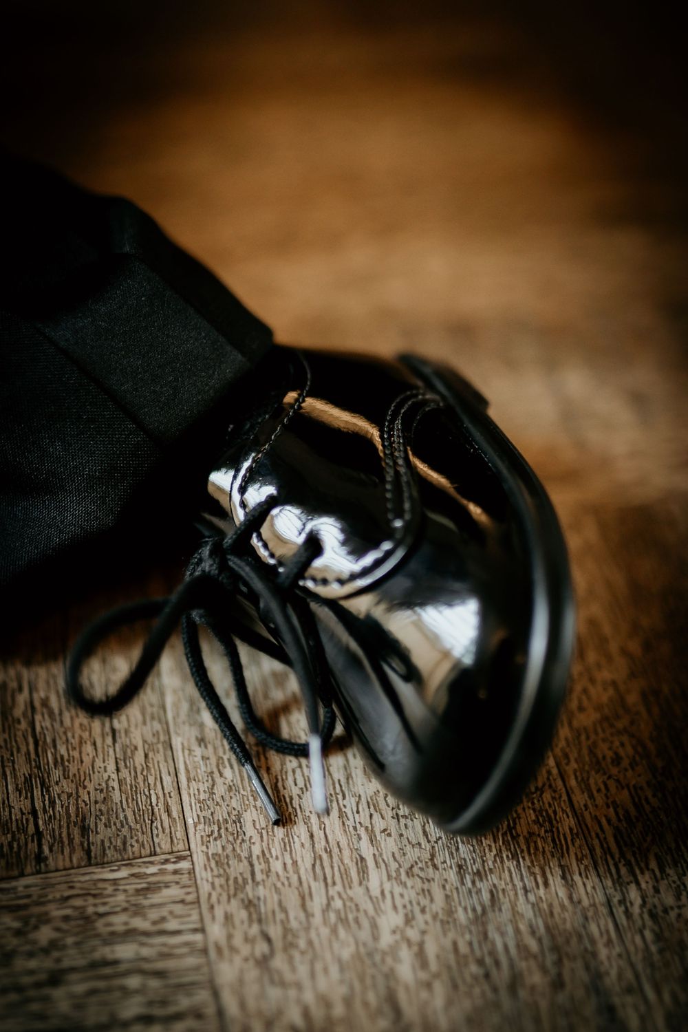 Close-up of shiny black formal dress shoes with laces on a wooden floor.