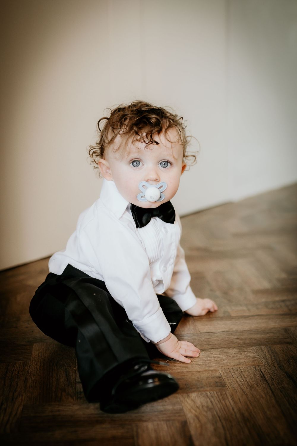 A sequence of shots showing a toddler in formal wear crawling on a hardwood floor.