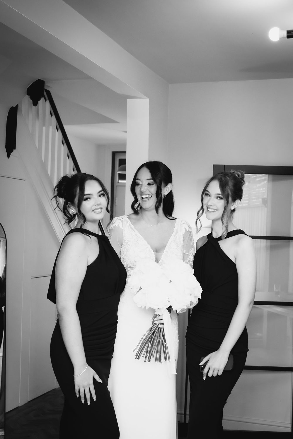 A bridal party poses together indoors with bridesmaids in black dresses flanking the bride in white.