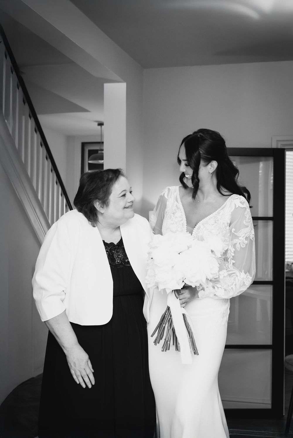 A bride and other women in black dresses sharing a joyful moment indoors.