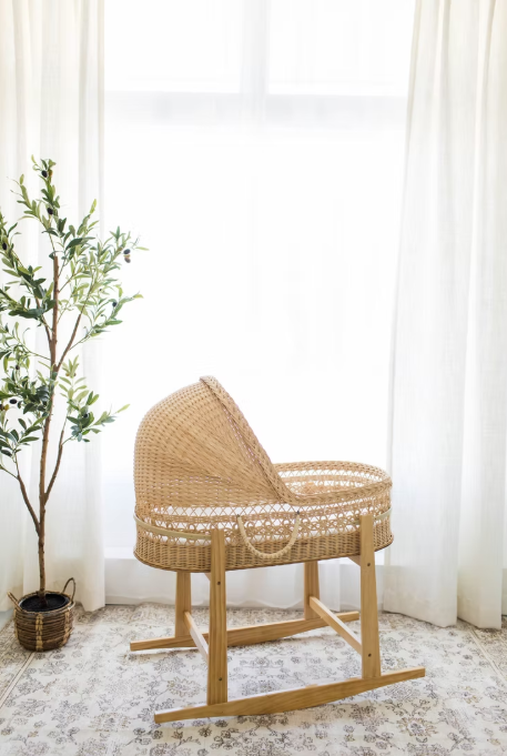 Natural rattan baby bassinet with curved wooden rocker base and white accents sits elegantly in a bright room.