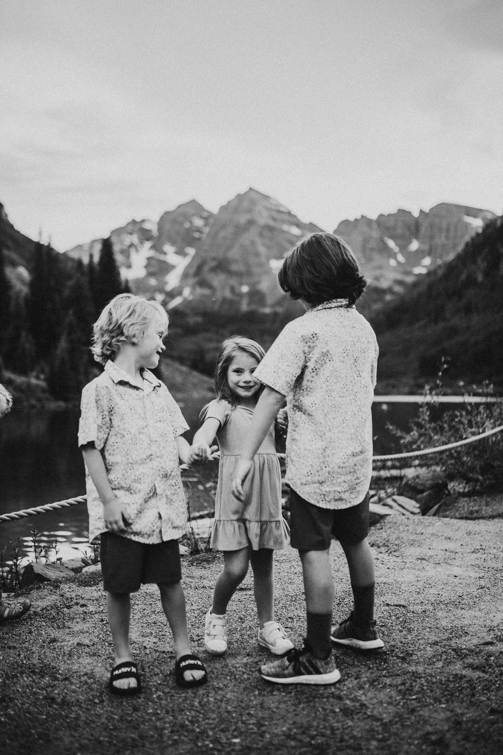Children stand together against a backdrop of majestic mountain peaks in a black and white outdoor landscape scene.
