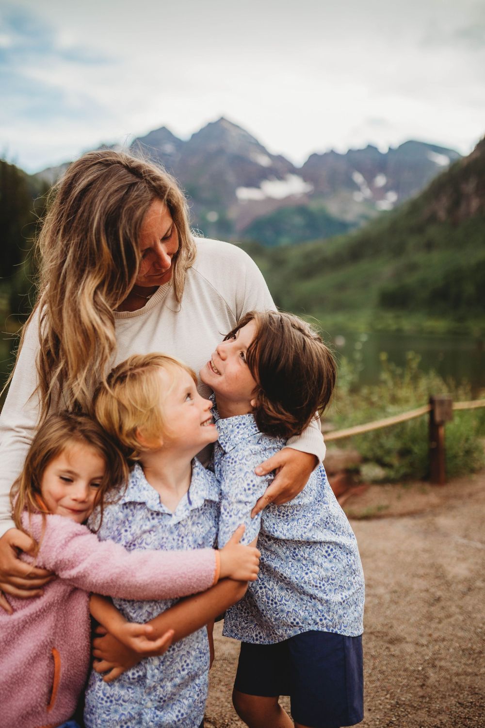 A loving family shares an intimate embrace while standing on a mountain trail with majestic peaks in the background.