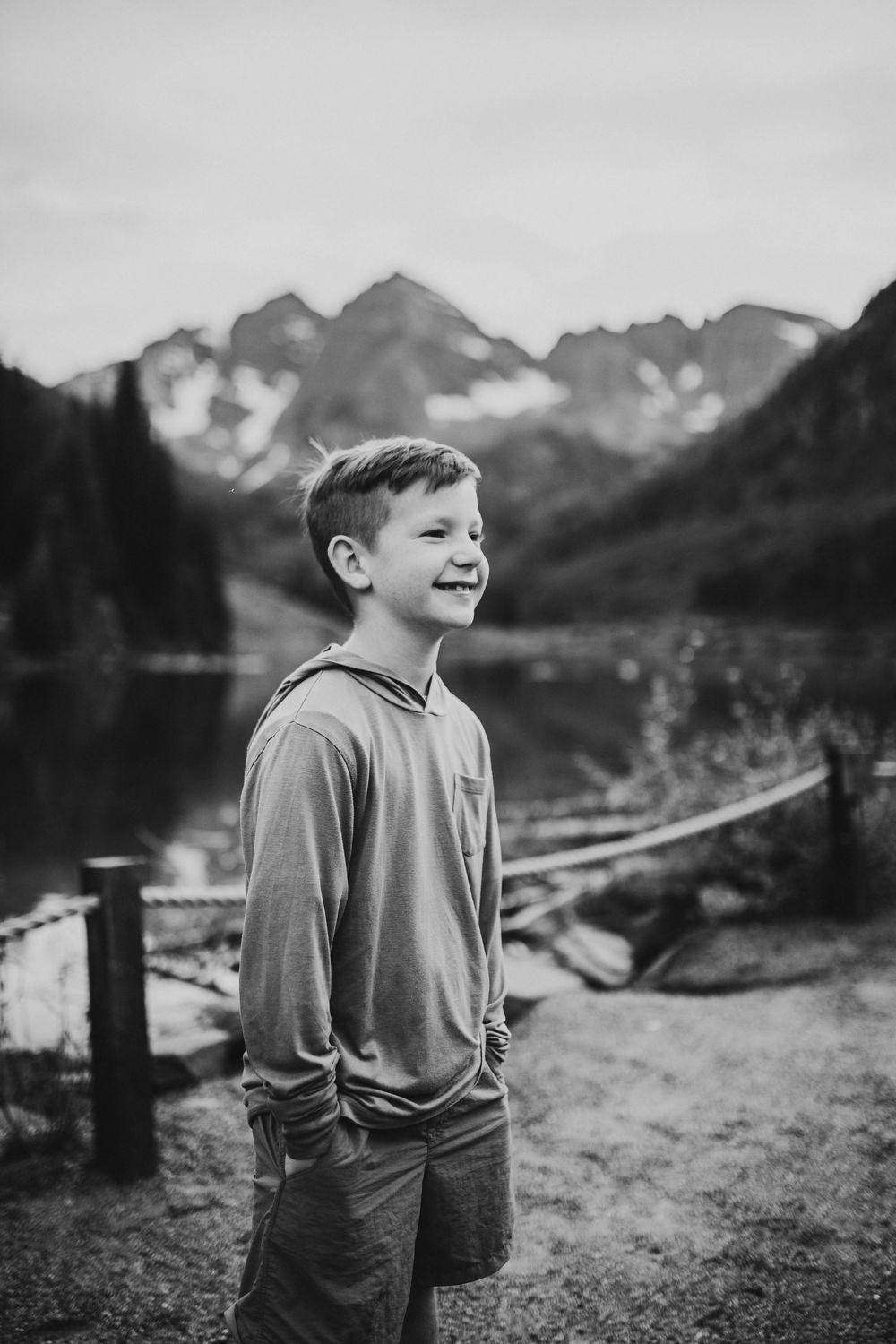 Black and white portrait of a joyful moment by a lake with snow-capped mountains in the background.
