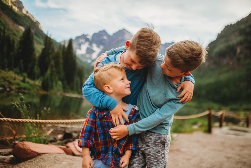 Family shares a joyful moment together while hiking in the mountains near a scenic alpine lake and peaks.