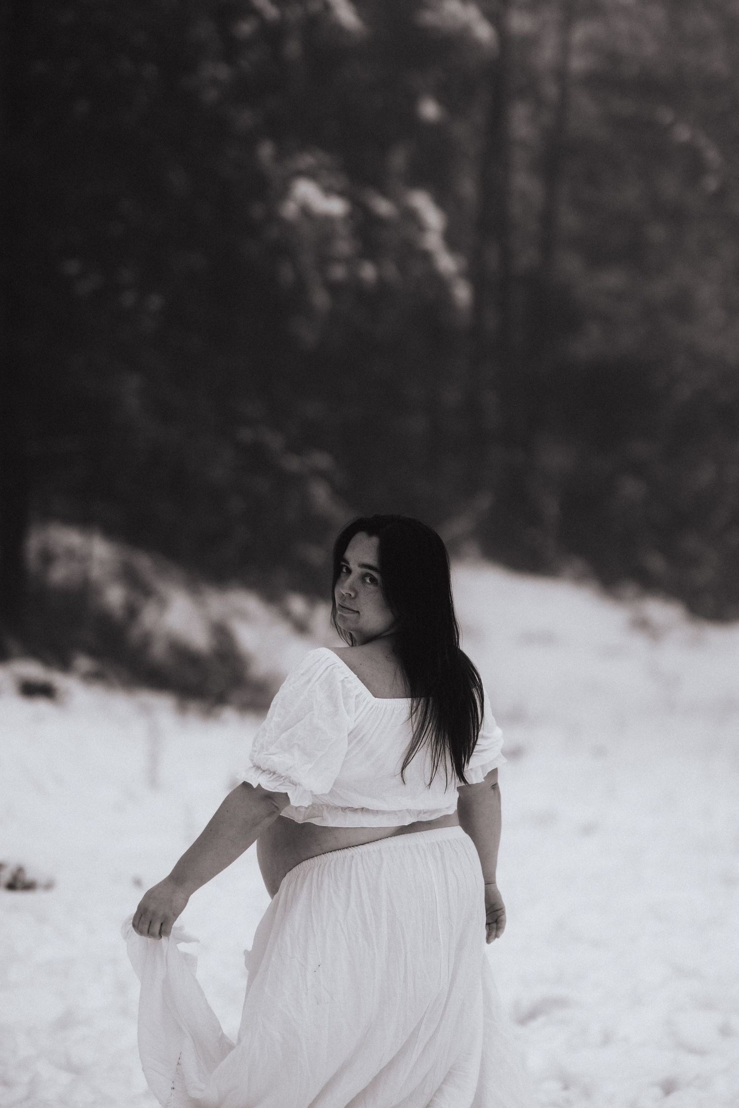 A graceful figure in a flowing white dress moves expressively against a dark woodland background creating an ethereal scene.