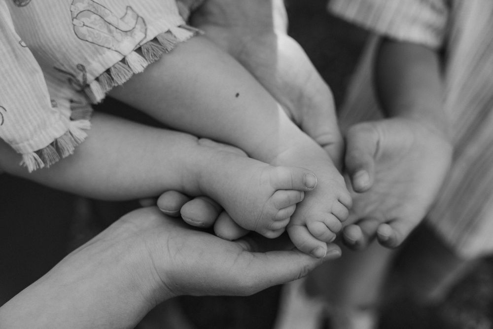 Nahaufnahme in Schwarzweiß von winzigen Babyfüßen, die sanft von Erwachsenenhänden gehalten werden.