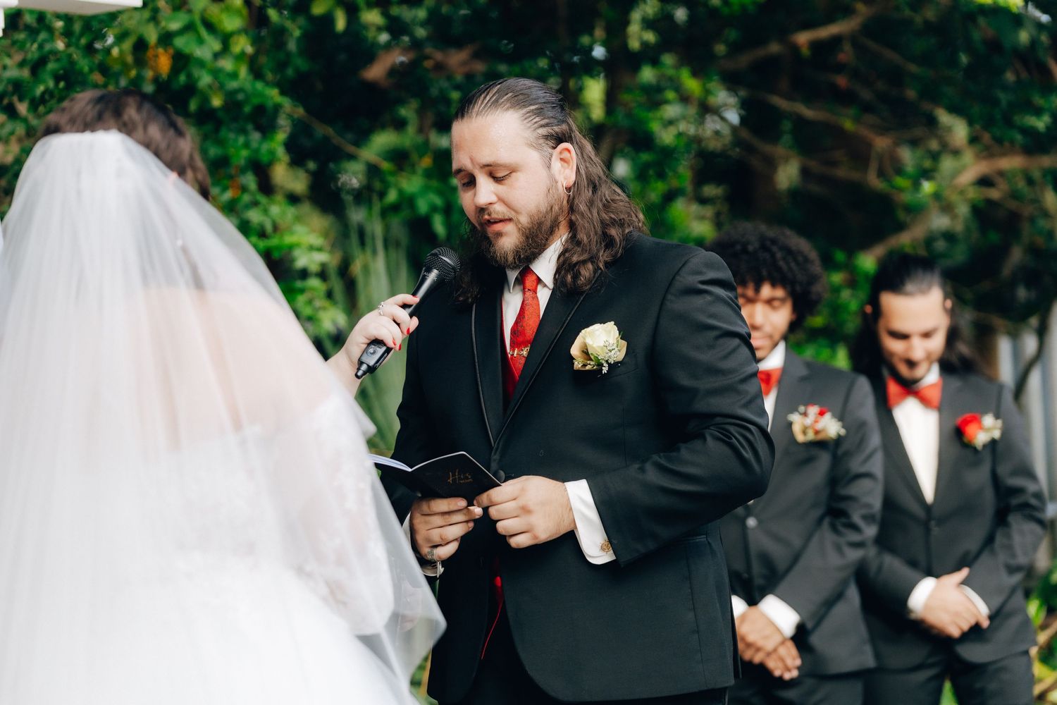 Wedding ceremony moment captured outdoors with lush greenery in the background.