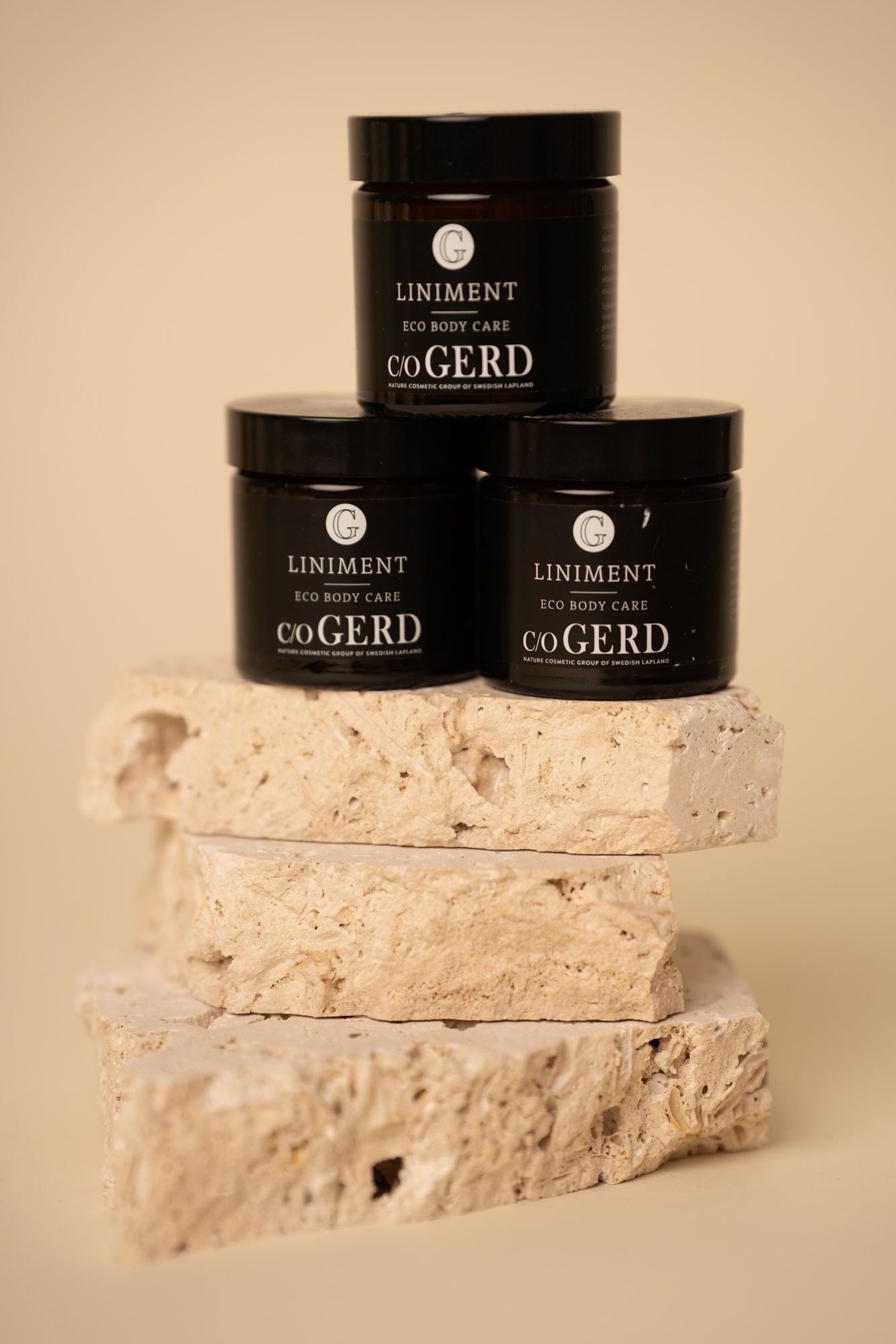 Black cosmetic jars from Uniment and coGERD brands displayed on textured white stone or mineral surfaces.