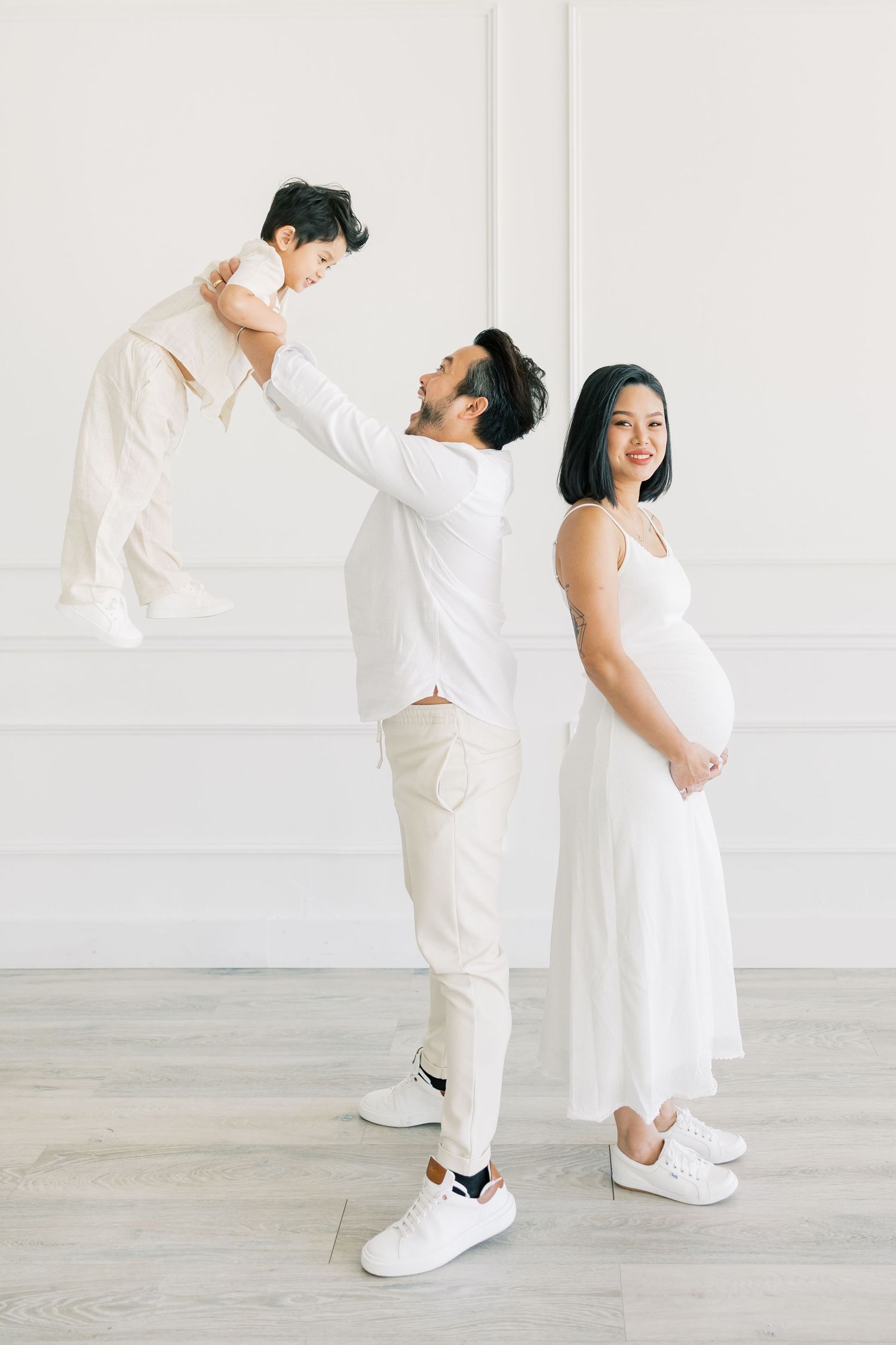 A family in white creates a playful pose with a pregnancy announcement theme.