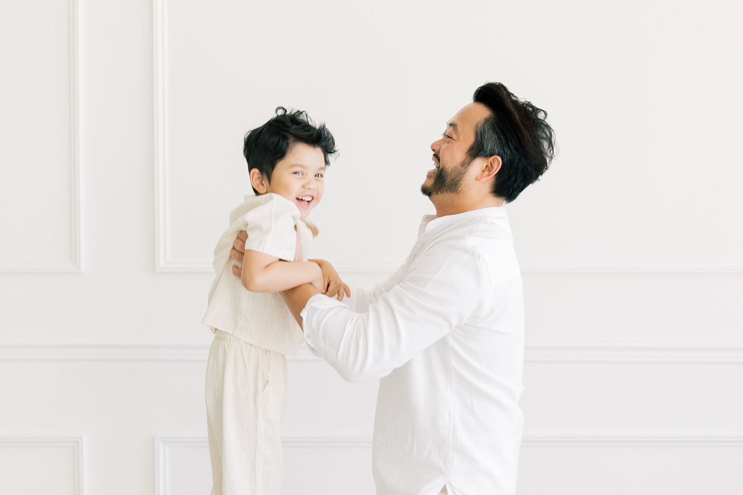 A joyful moment between parent and child, both wearing white against a bright wall.