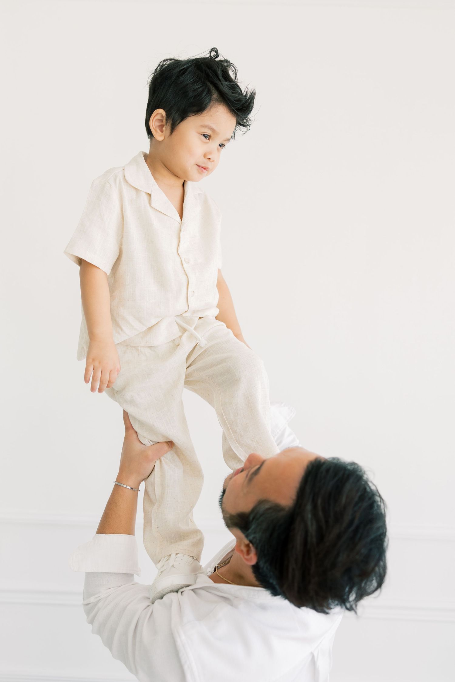A tender moment captured as a parent lifts a child wearing all white against a bright minimalist background.